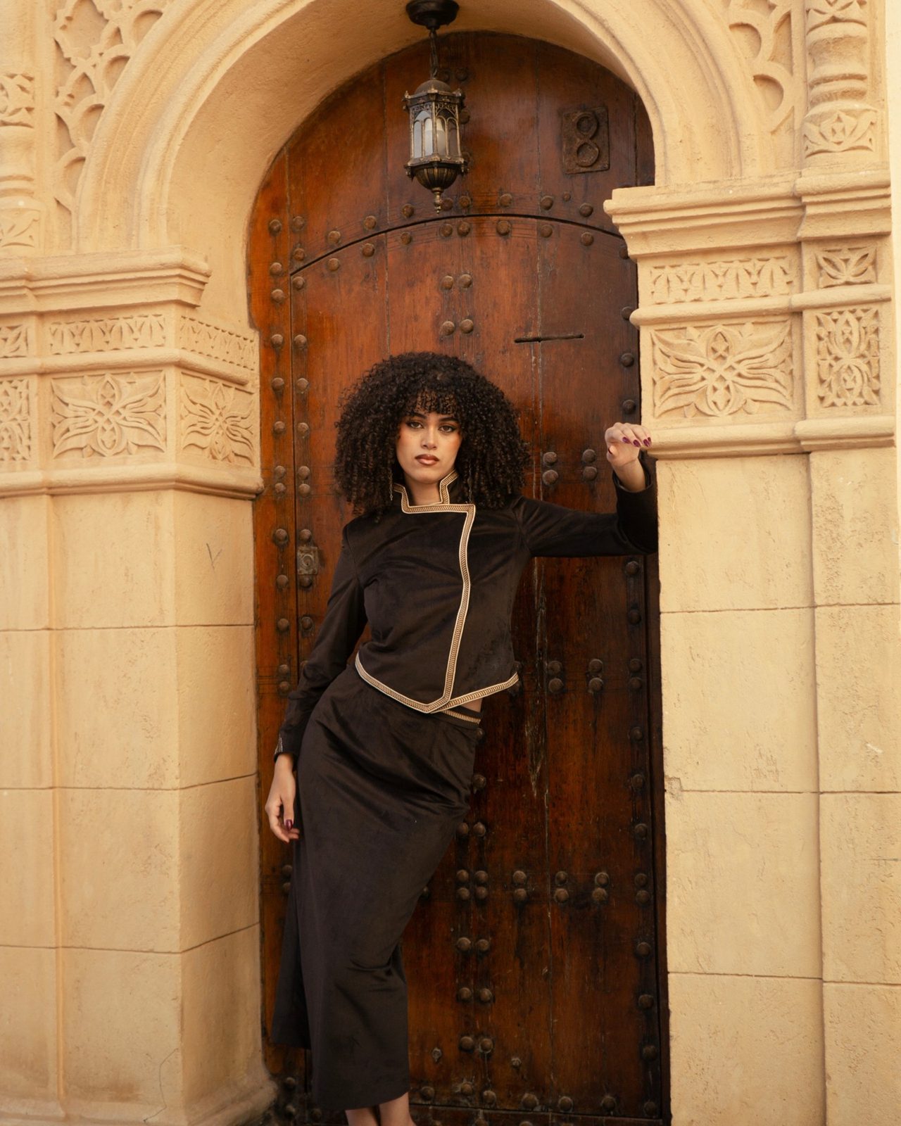Second Layer: chocolate velvet jacket with gold braid, in a carved doorway