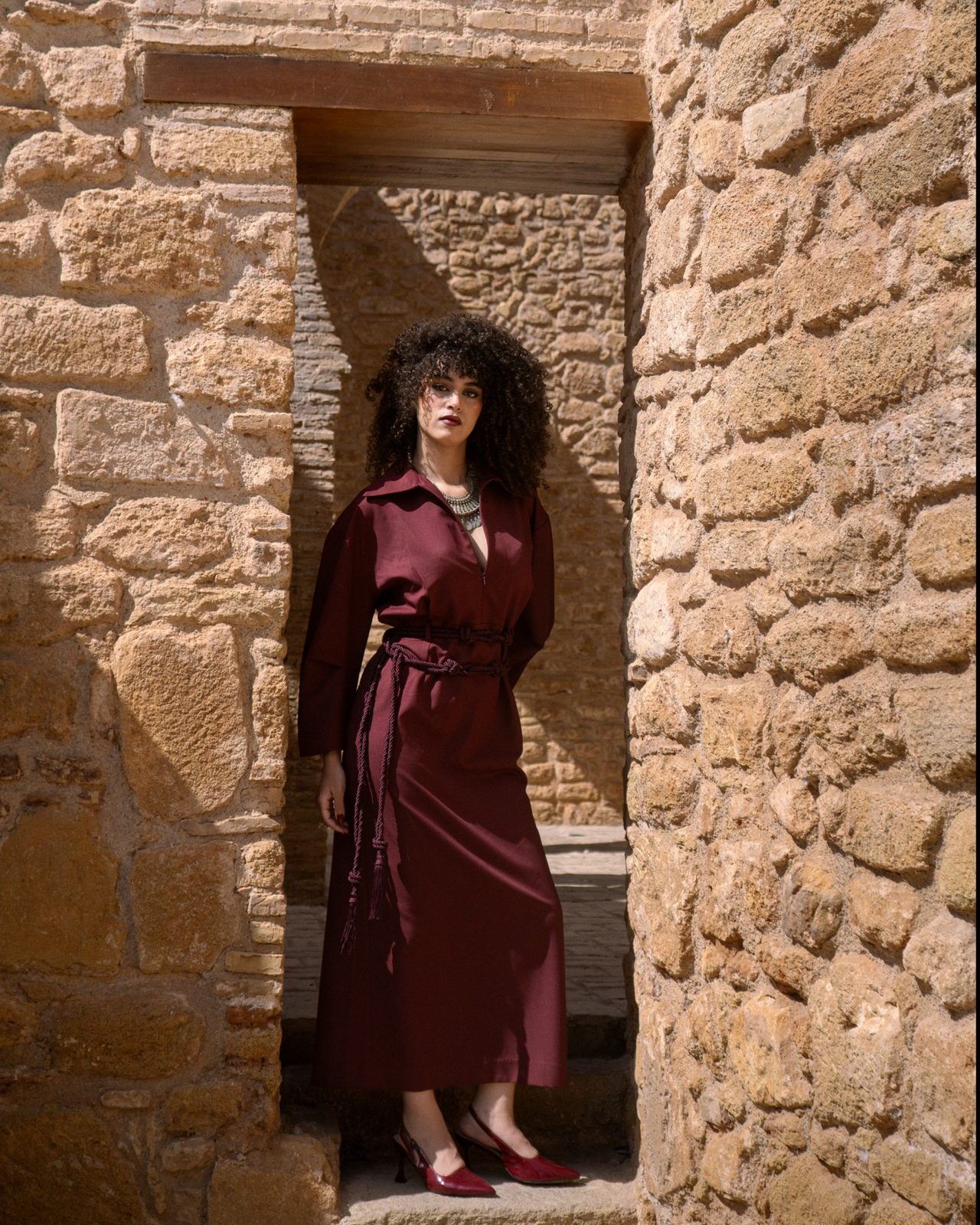 Third Layer: burgundy shirt dress with rope belt in a stone passage